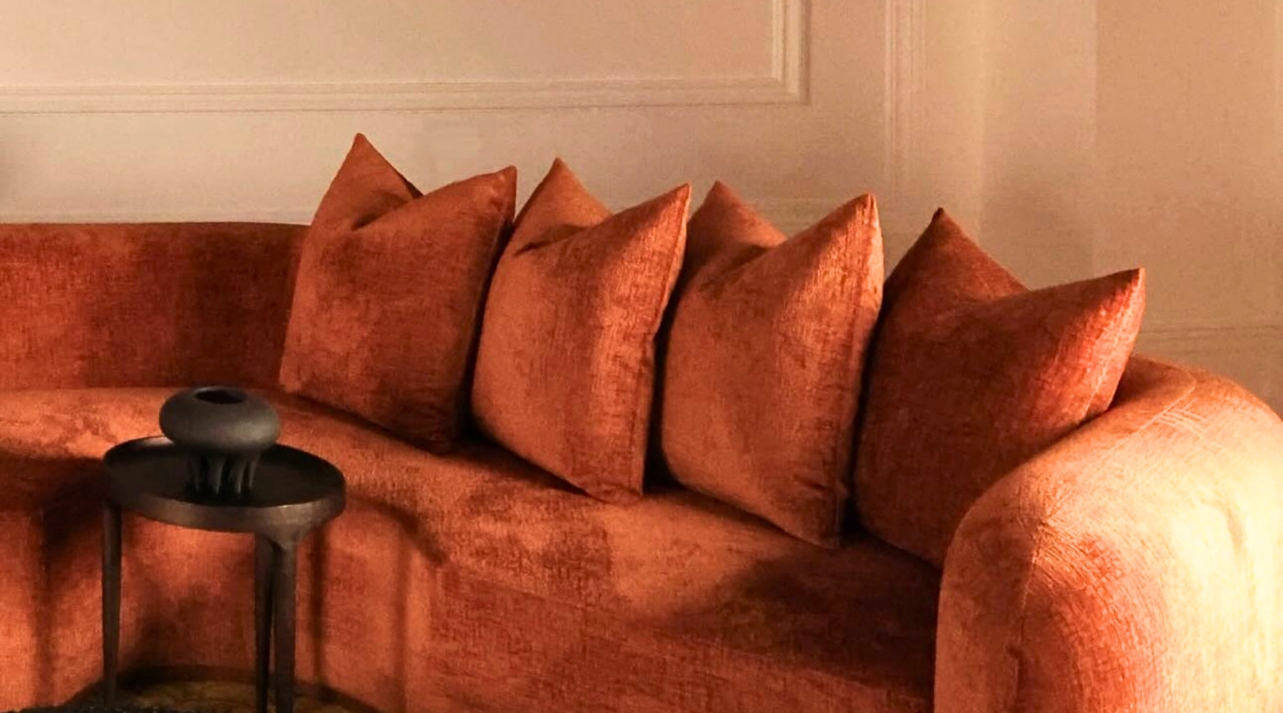 Orange sofa with decorative pillows against a neutral wall.